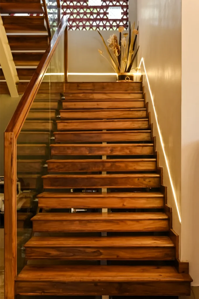 Wooden staircase with warm lighting and glass railing – Avanti Residence Thrissur