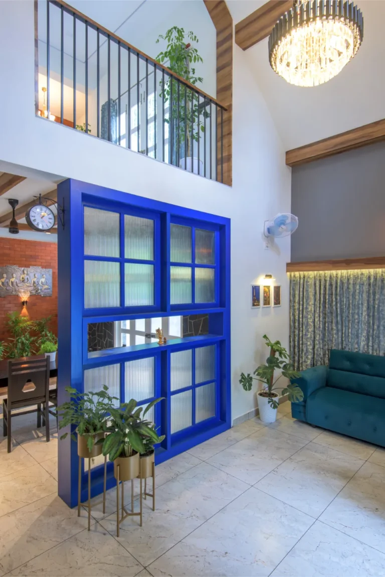 Double-height living space with chandelier and blue partition – Castle Residence Thiroor