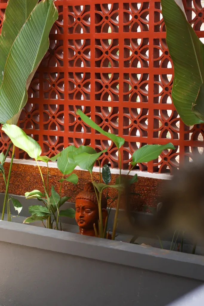 Buddha head sculpture among plants and terracotta wall – Courtyard House Wadakkanchery
