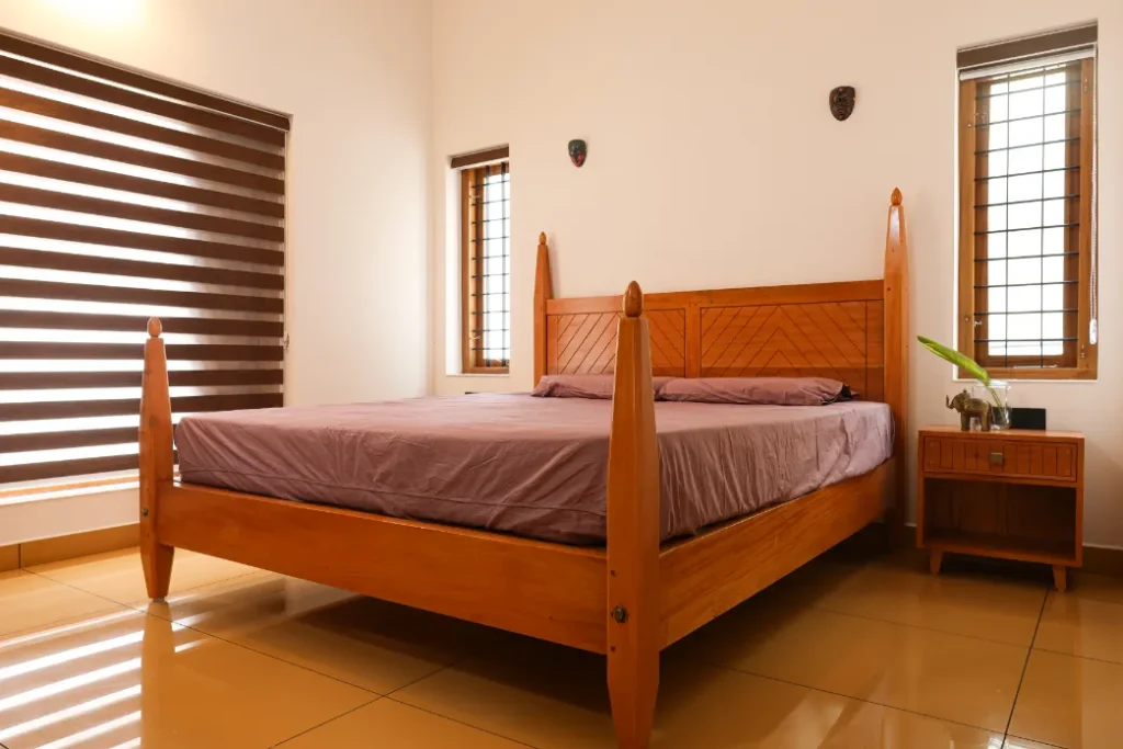 Bedroom with wooden bed and muted purple bedding – Courtyard House Wadakkanchery