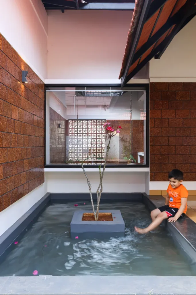 Child playing near water courtyard with flowering tree – Courtyard House Wadakkanchery