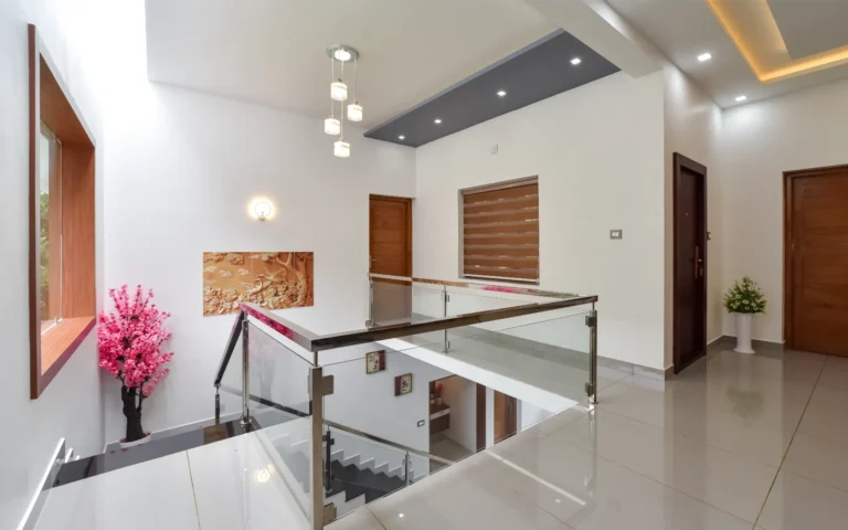 Staircase landing with glass railing and pink decor – Varghese Residence Wadakkanchery