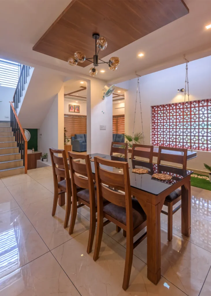 Dining area with wooden chairs and swing beside jali wall – Vasudevam Residence Chalakudy