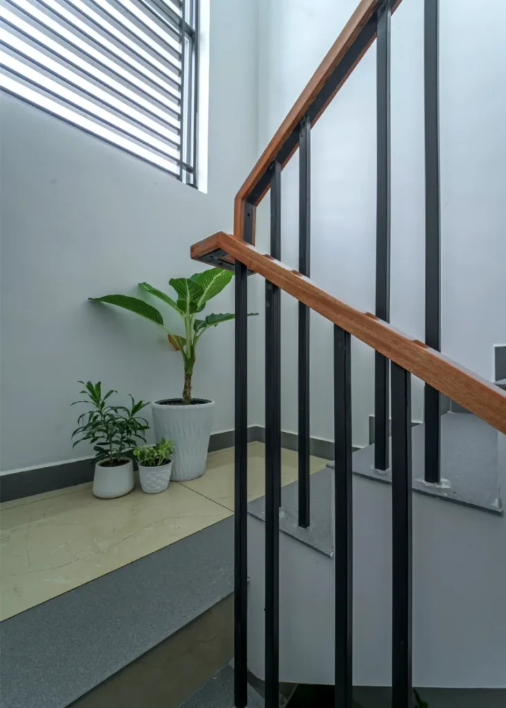 Staircase detail with black railing and indoor plants – Vasudevam Residence Chalakudy