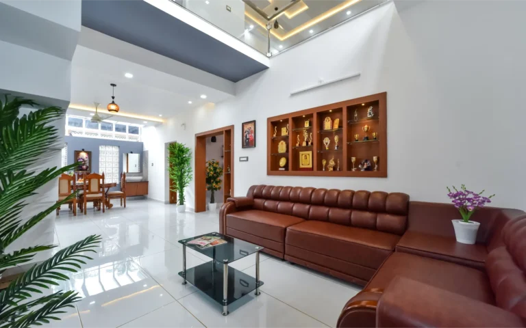 Living area with brown leather sofa and glass staircase – Varghese Residence Wadakkanchery